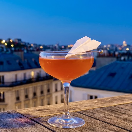A vibrant orange-hued Paper Plane cocktail served in a coupe glass.